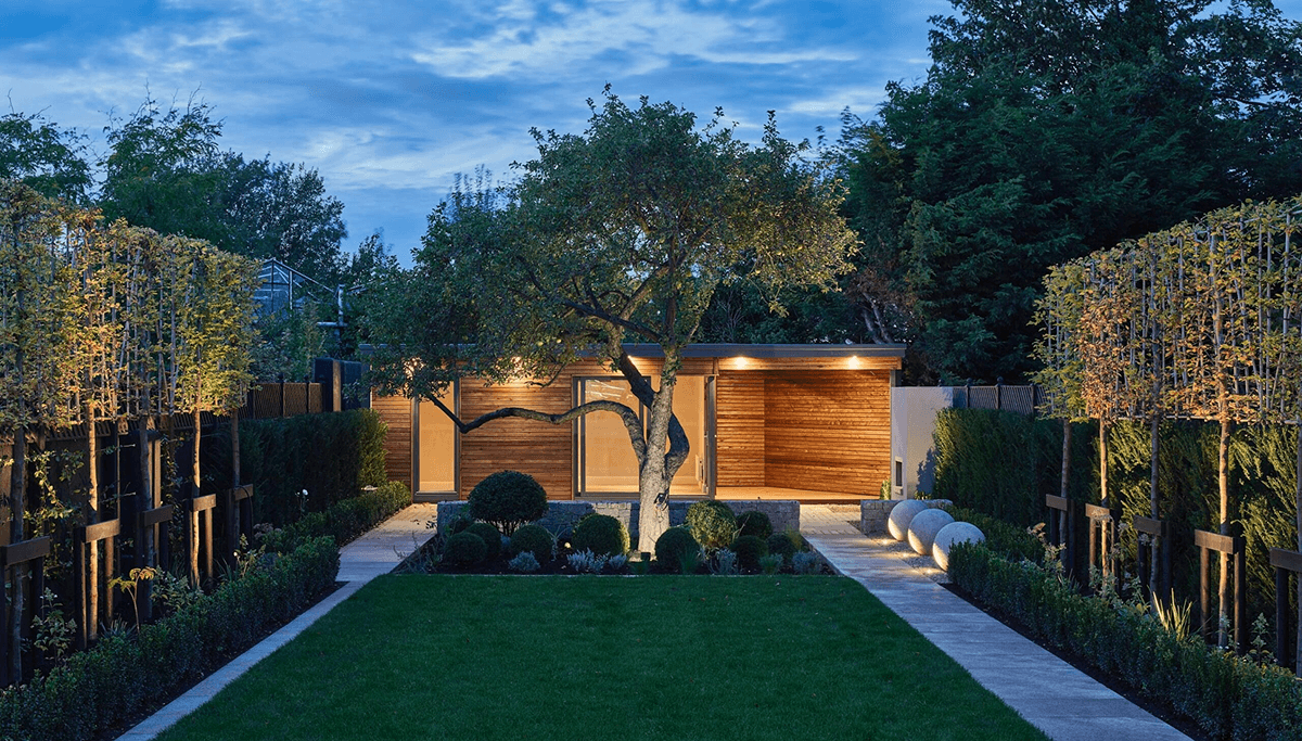 A Shomera garden studio lit at dusk in a landscaped garden