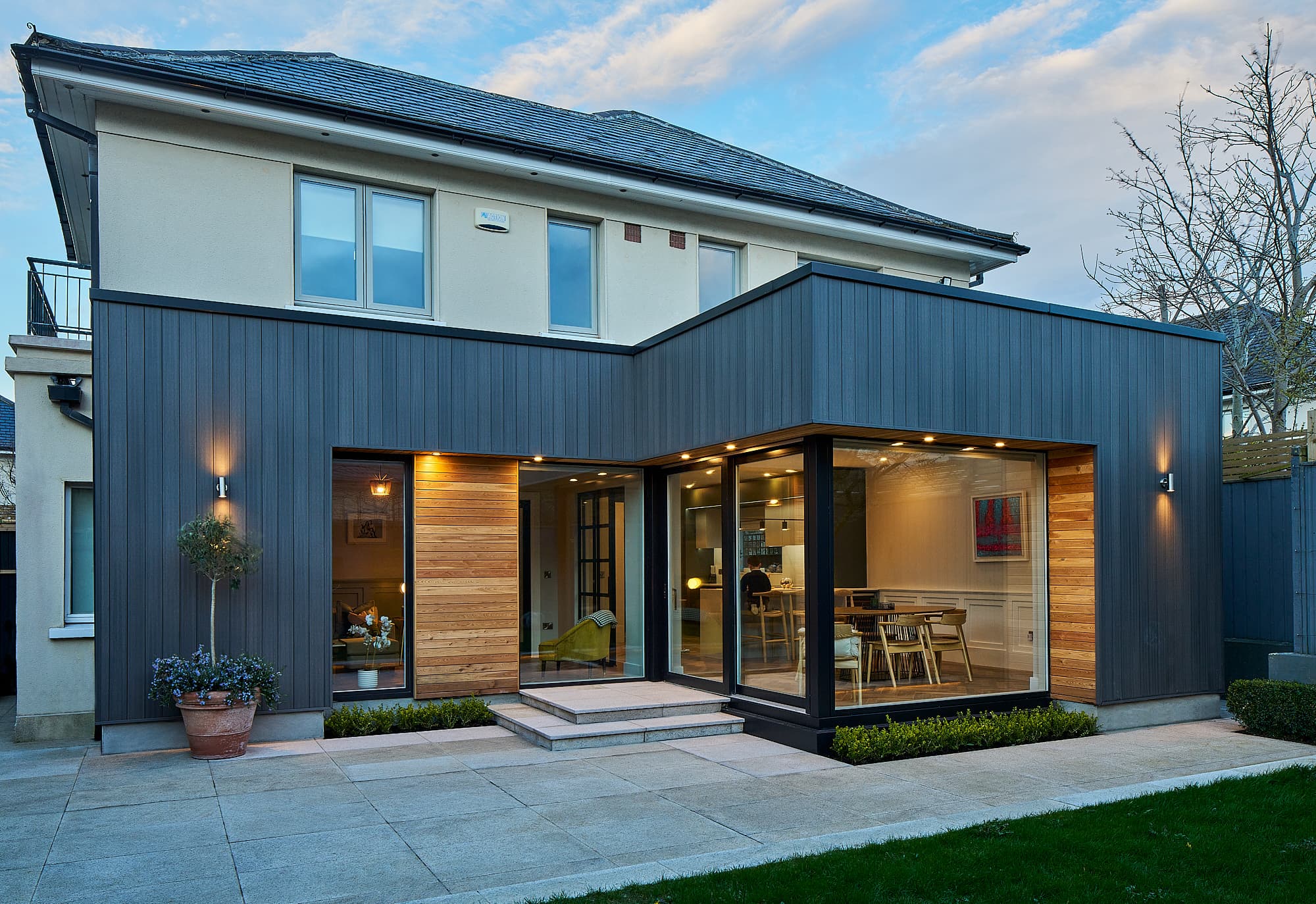 The rear of the Carrickmines house at dusk, the extension glowing behind full-height glazing