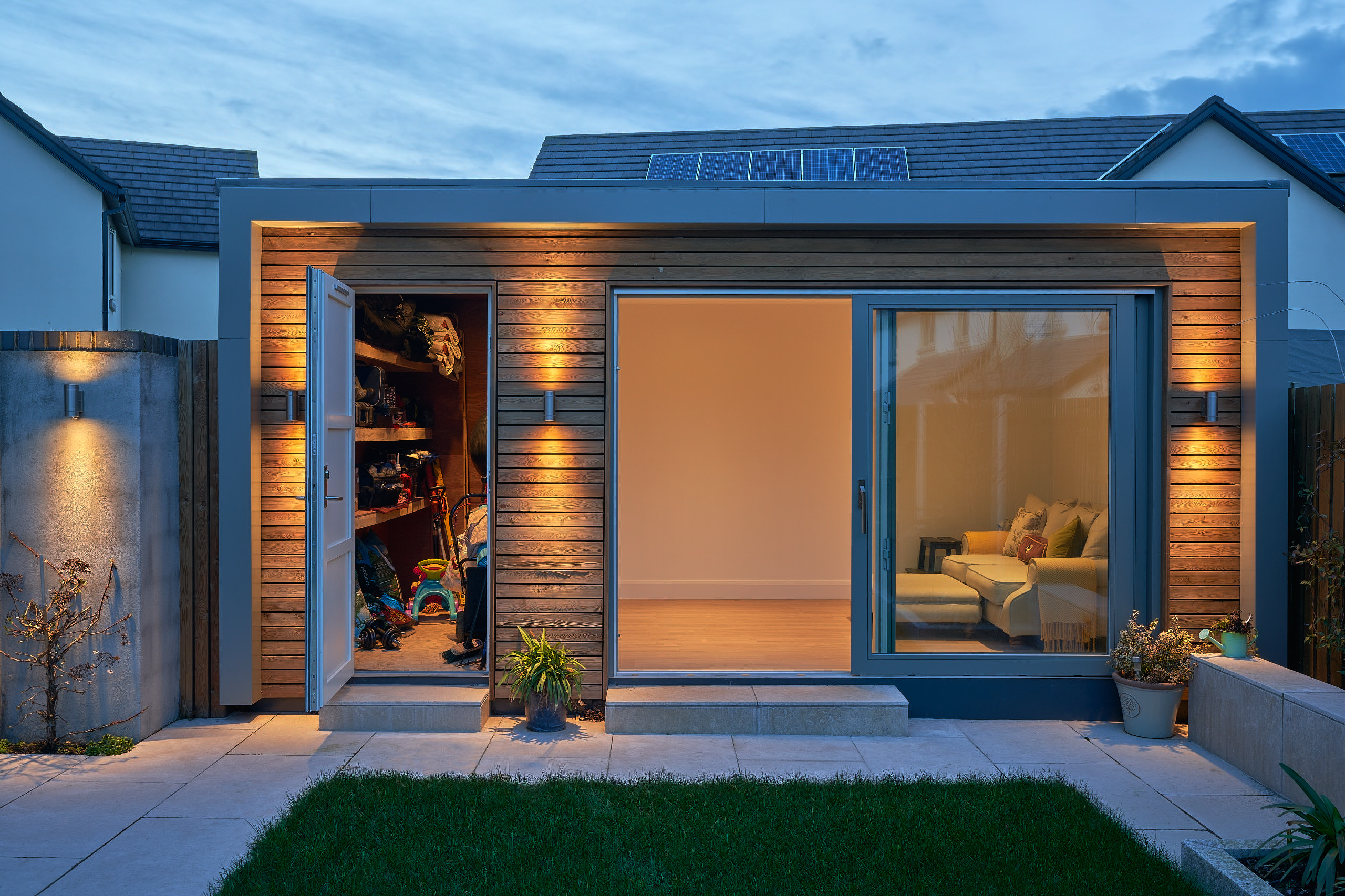 The studio at dusk with the storage bay open beside the lit lounge, the whole elevation uplit