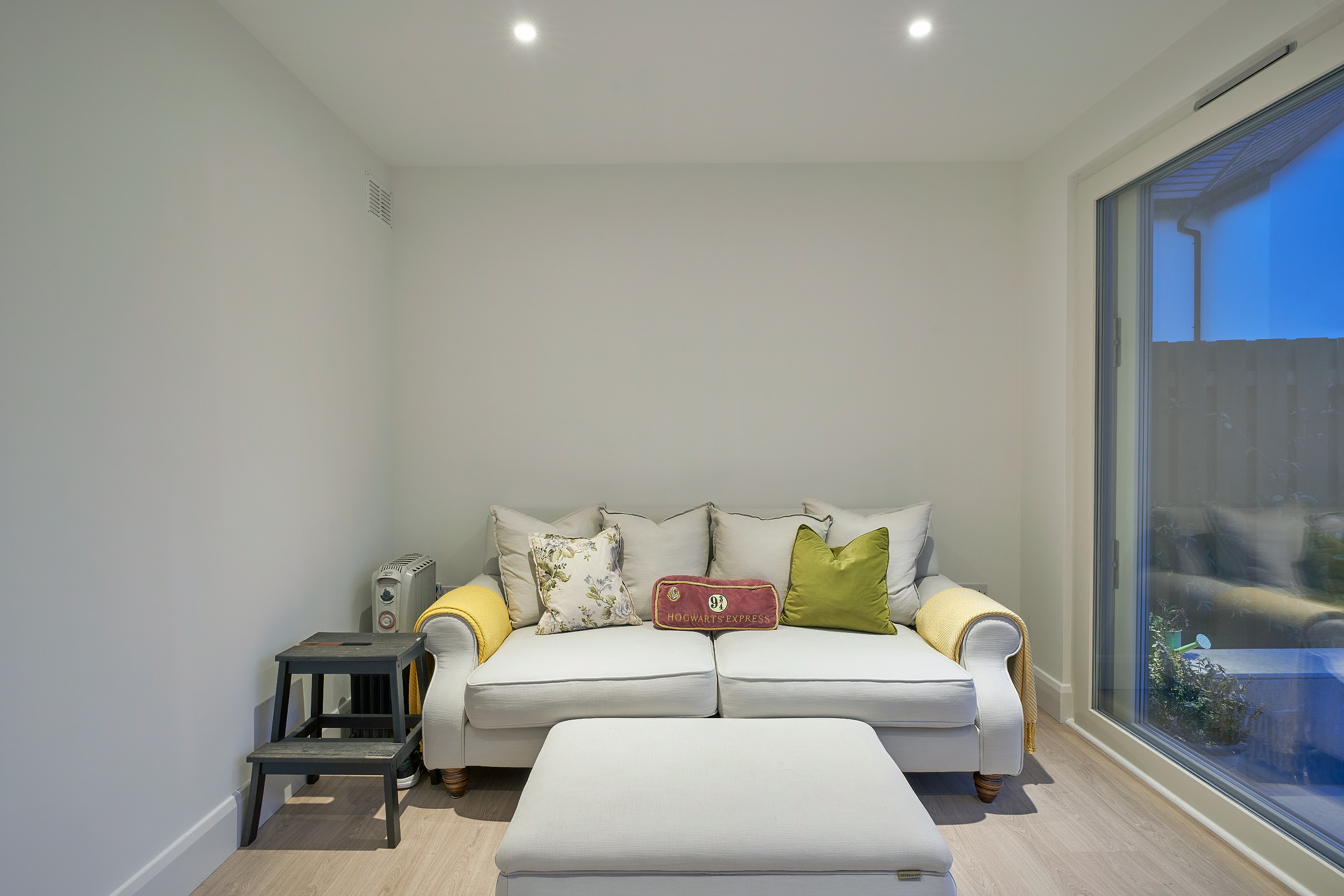 Inside the studio, a white sofa and footstool beside the full-height glazing