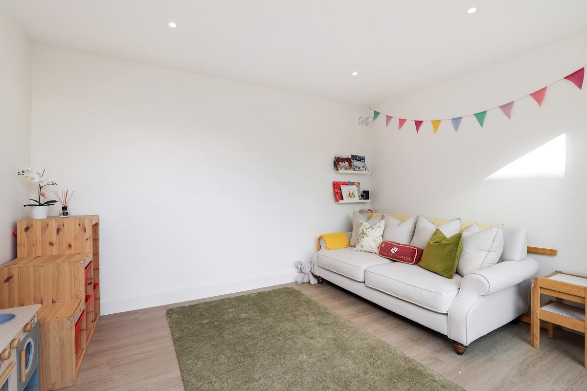 Inside the studio, a white sofa and low storage beneath bunting, with a green rug on the floor