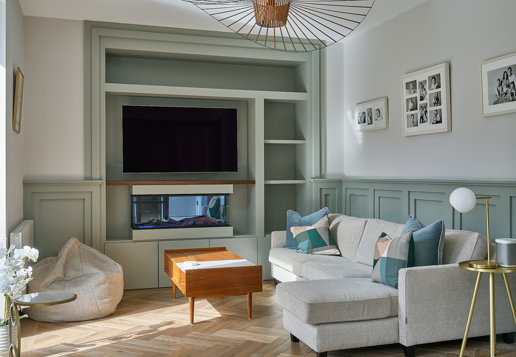 The family room, with sage-green panelling, built-in shelving and a wall-mounted screen above the fireplace