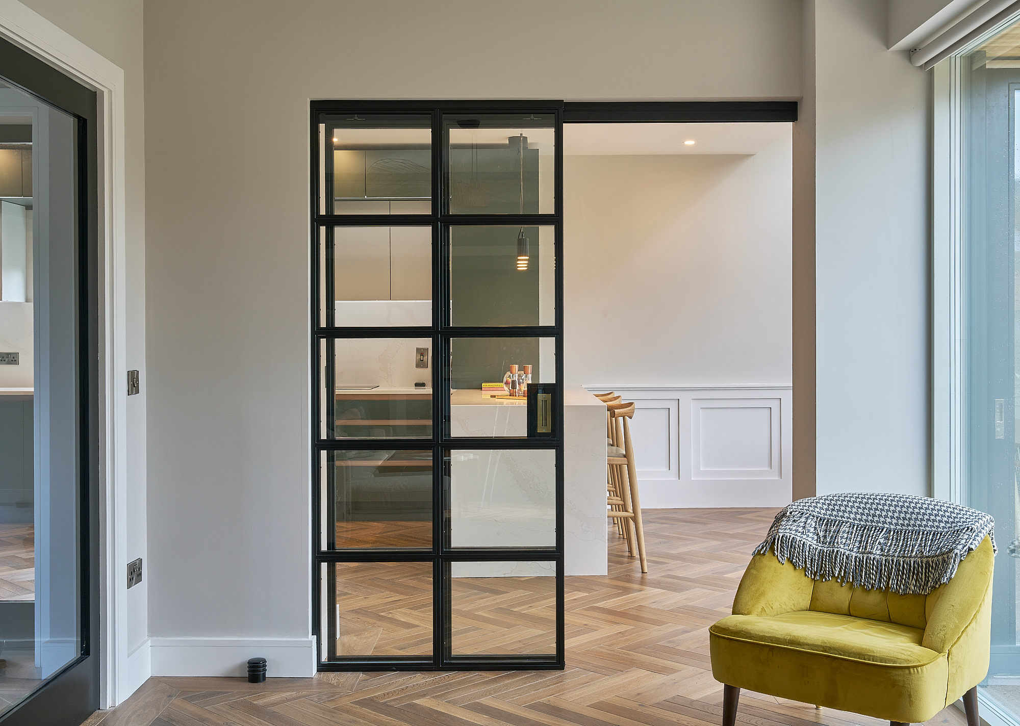 Crittall-style glazing between hallway and kitchen, with a mustard armchair in the foreground