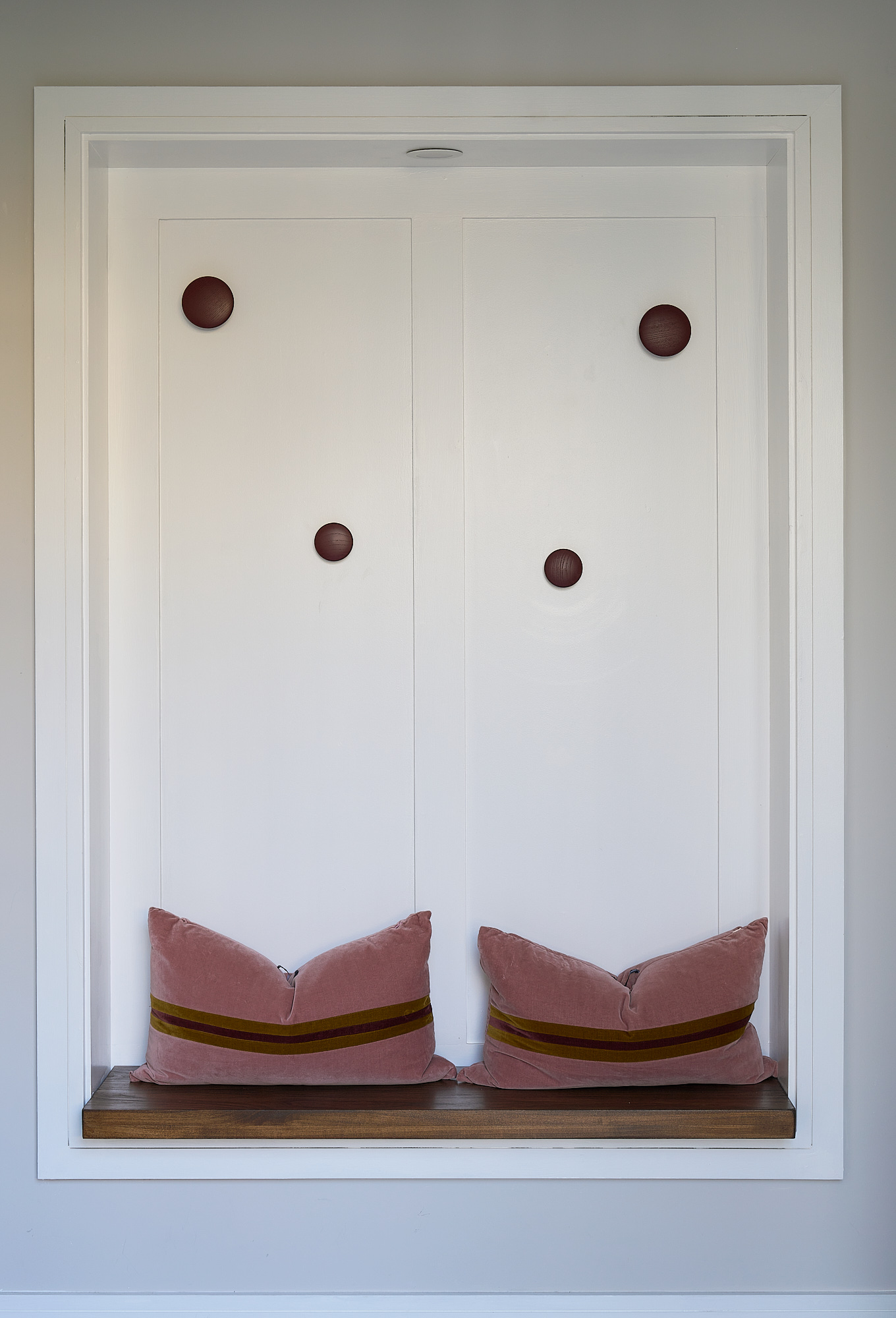 The porch window seat, upholstered in pink and set into a panelled niche with coat hooks above
