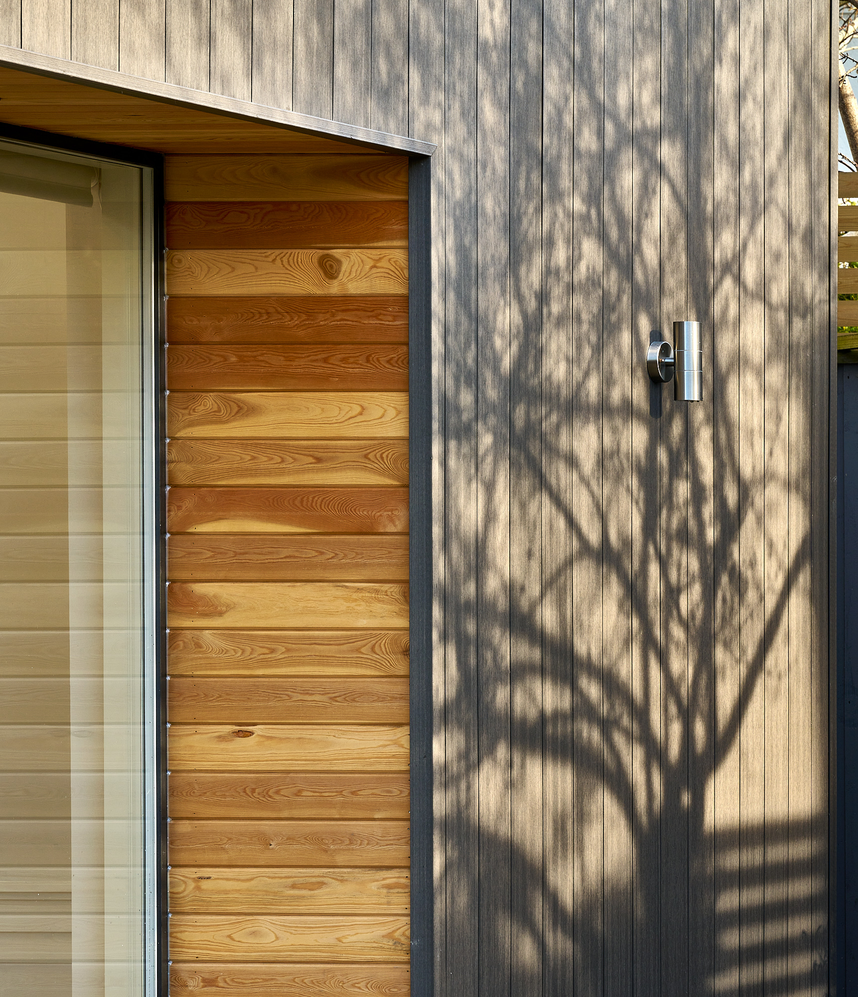 Cedar cladding and a timber door on the rear elevation, tree shadows falling across the boards