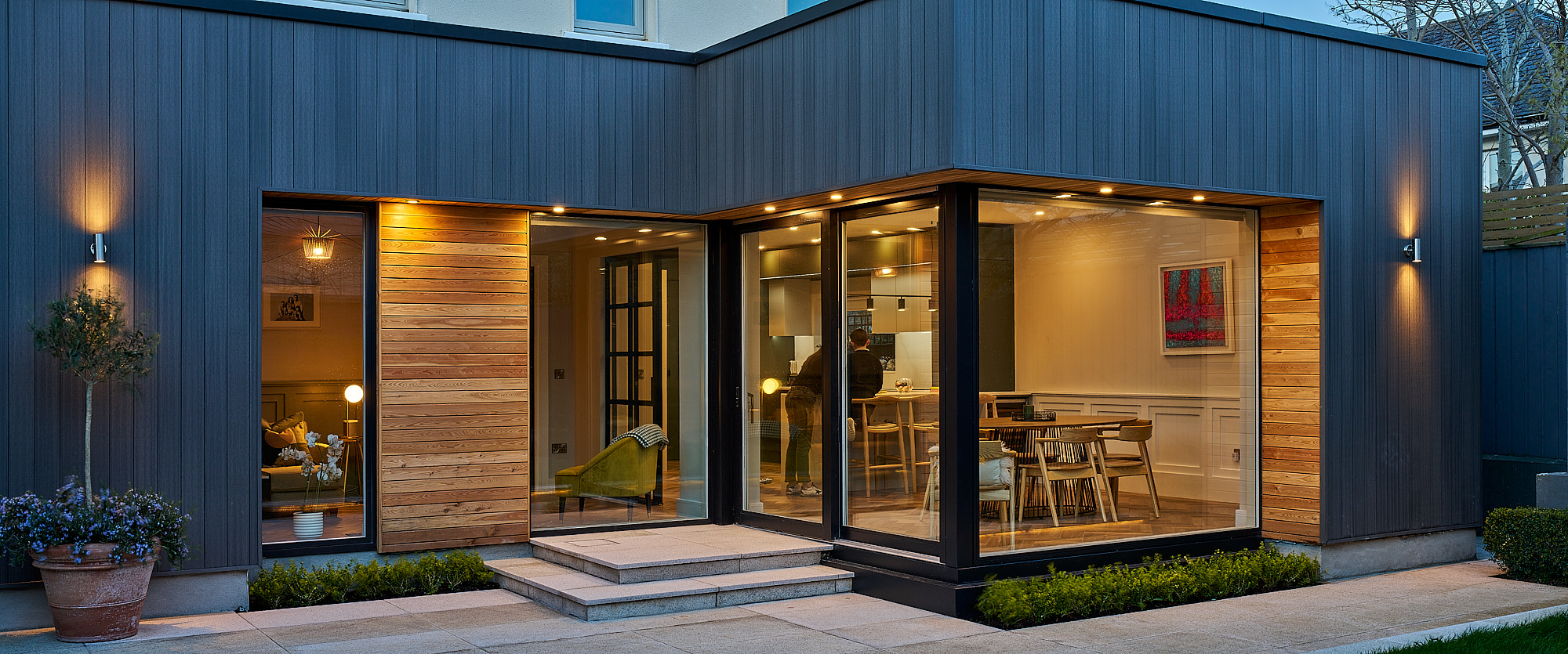 A wide view of the rear elevation at dusk, extension and patio lit end to end