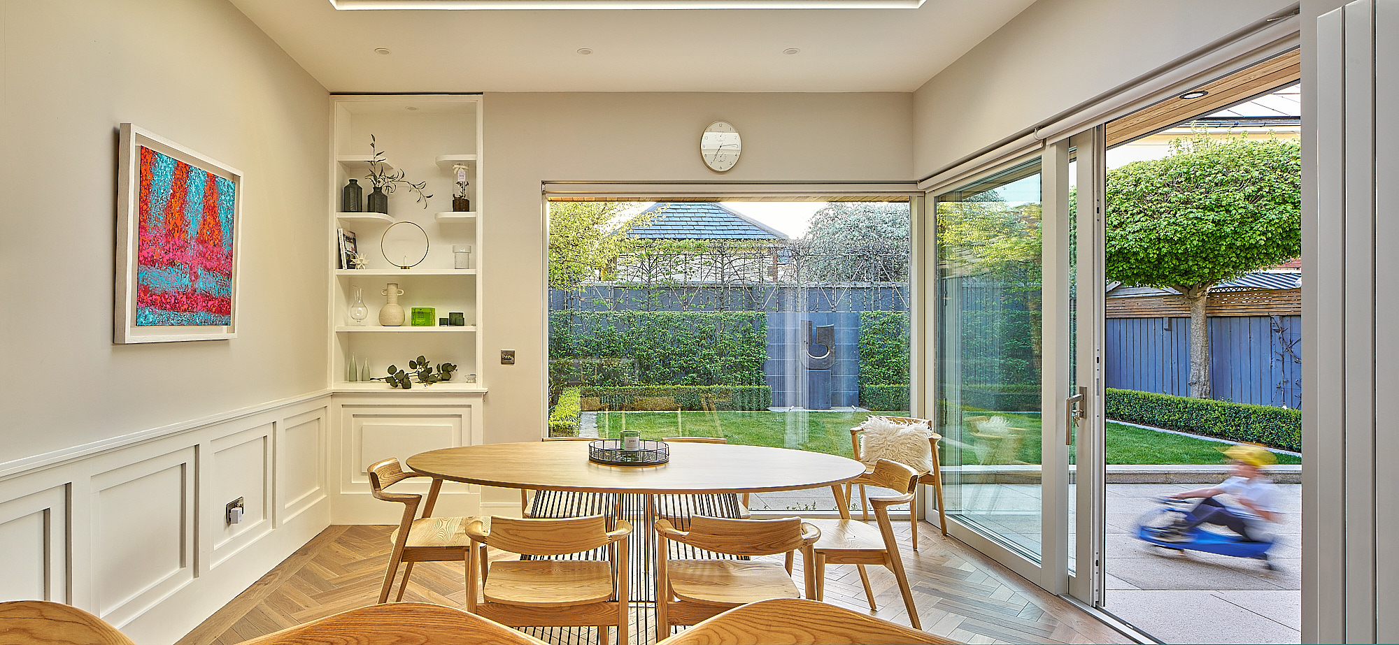 The dining table beside the garden glazing, with a child playing on the patio outside