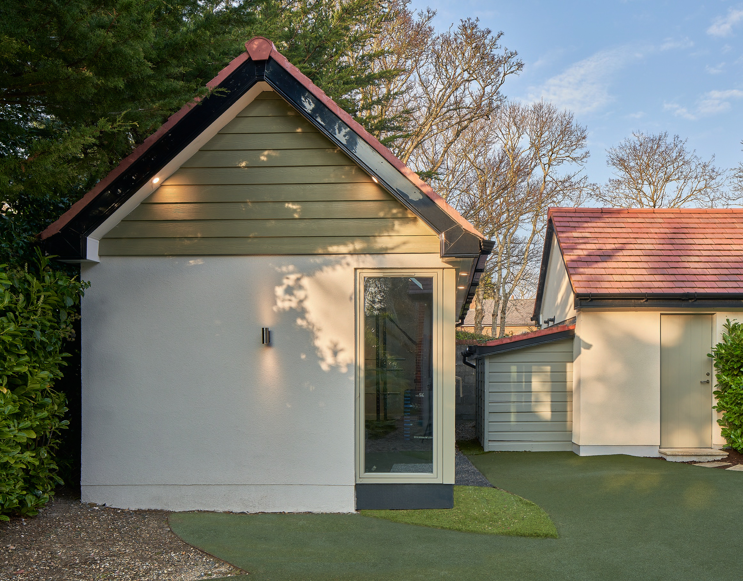The garden gym studio, its apex roof and rendered walls set against clipped hedging and lawn