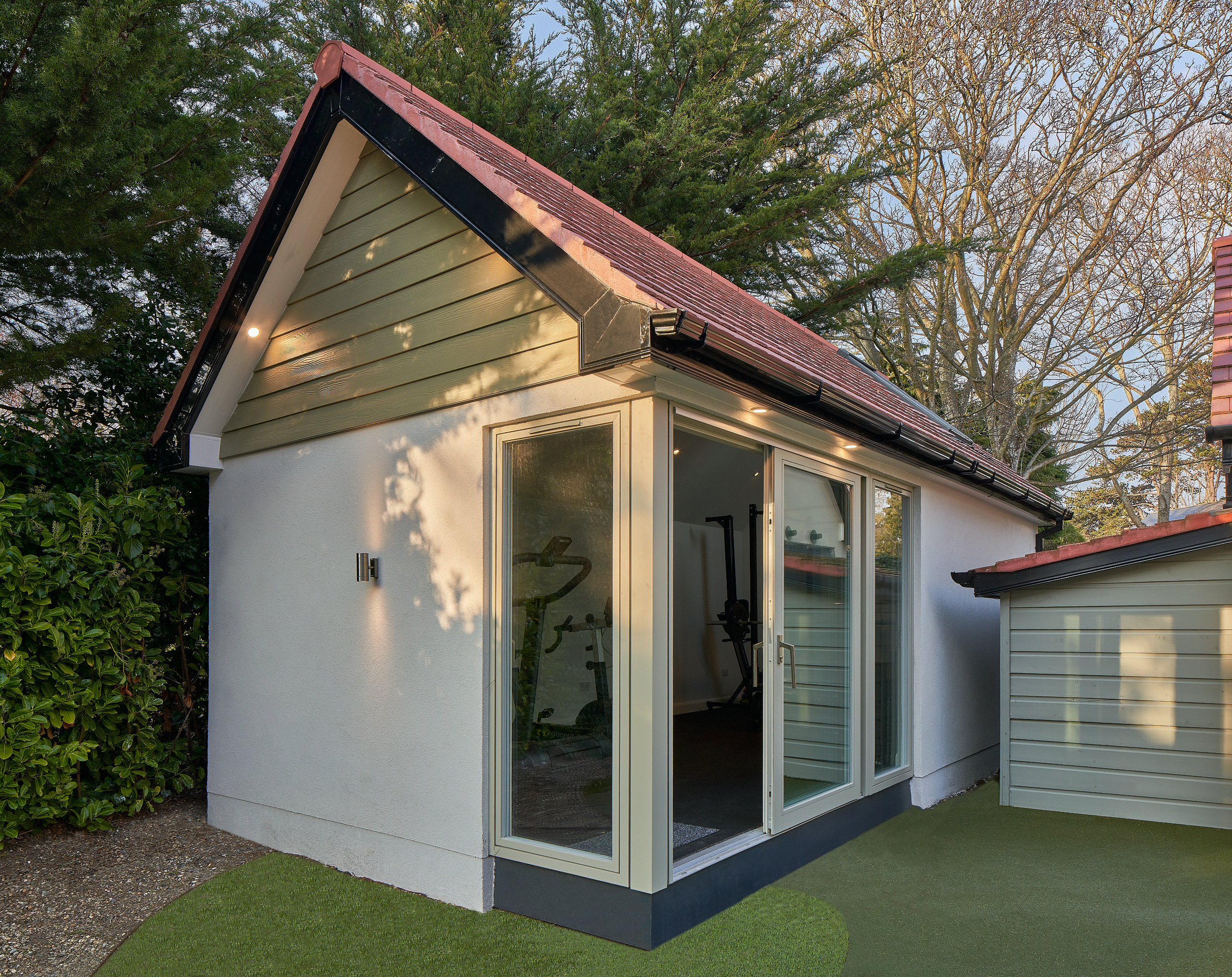 The studio's glazed corner, gym equipment visible inside beneath the apex gable