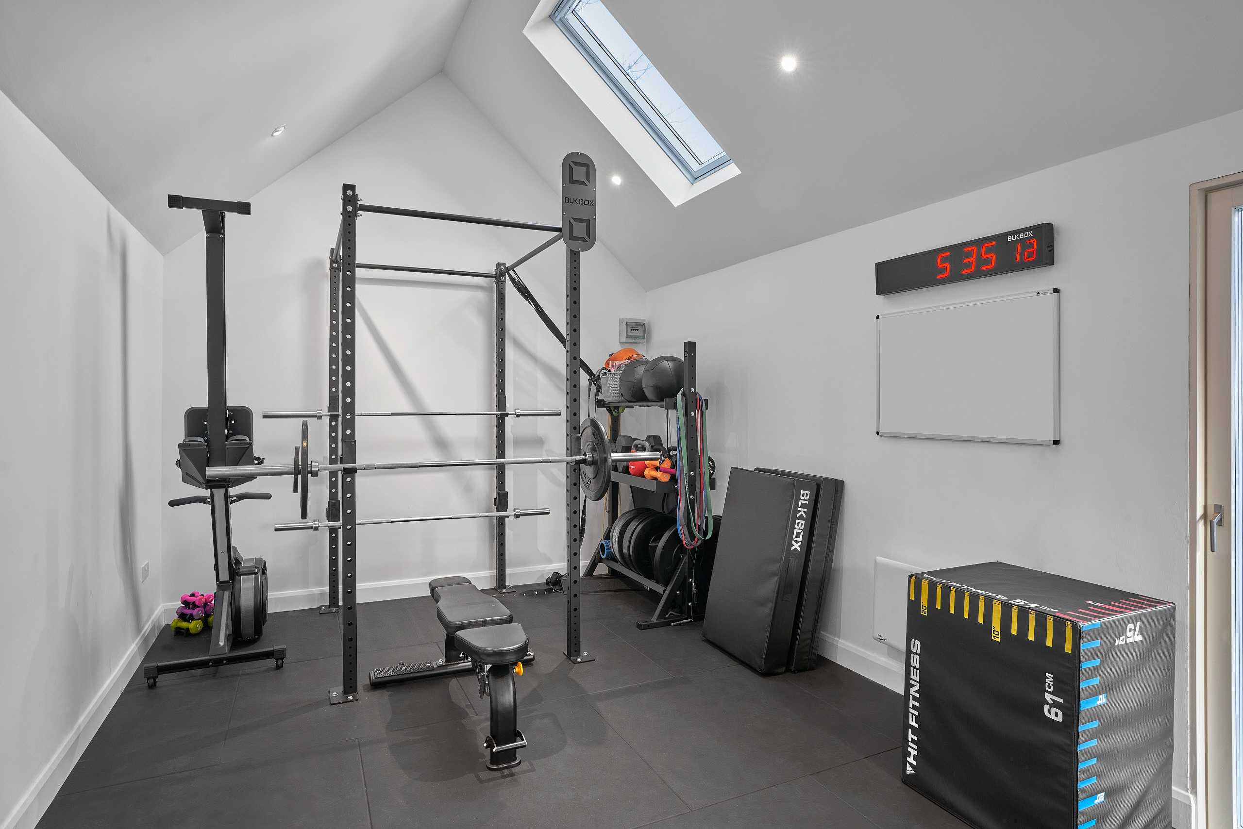 Inside the gym, a squat rack, weights bench and plyo boxes beneath a rooflight