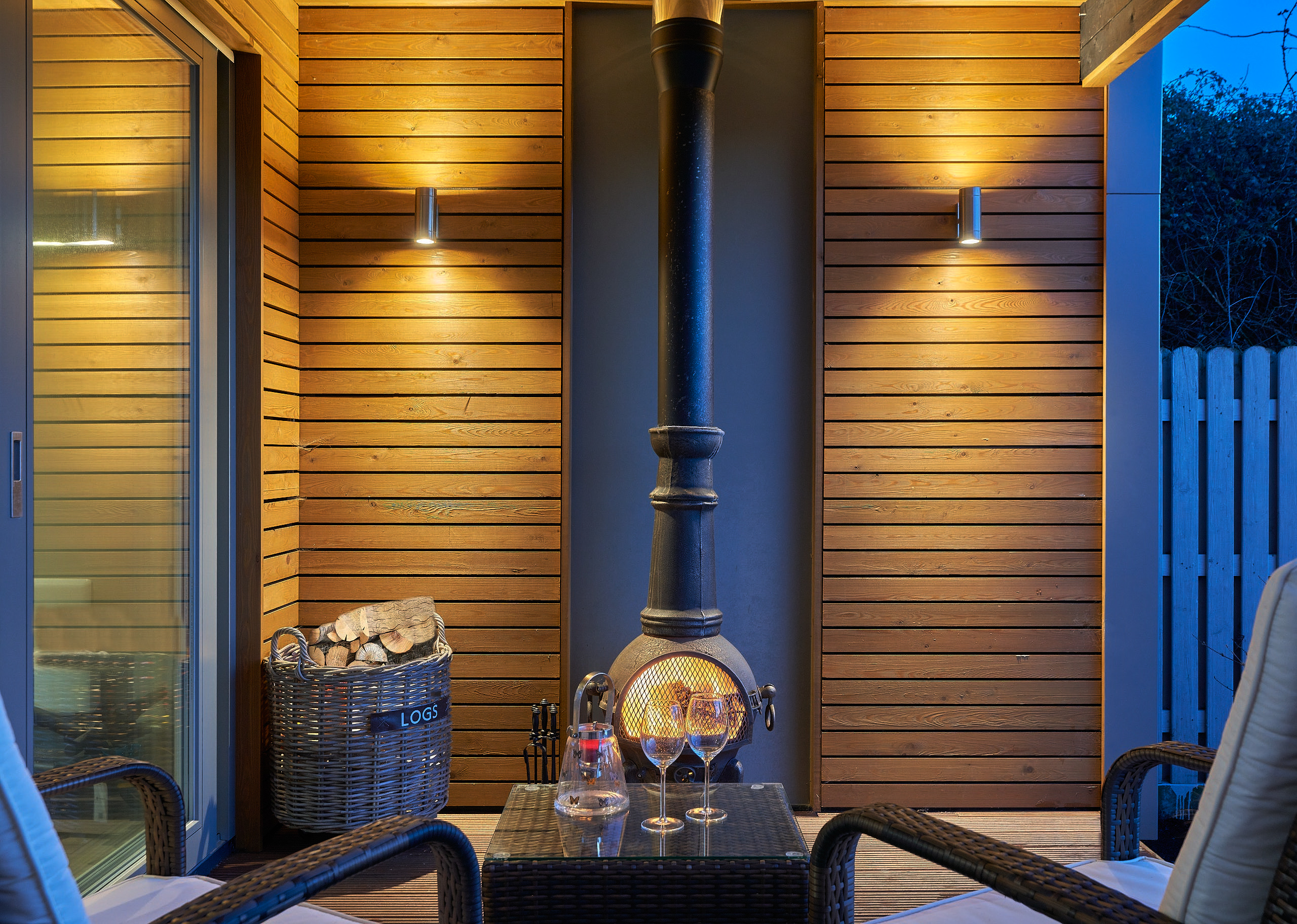 The covered terrace at dusk, a wood-burning chiminea and seating against the cedar wall