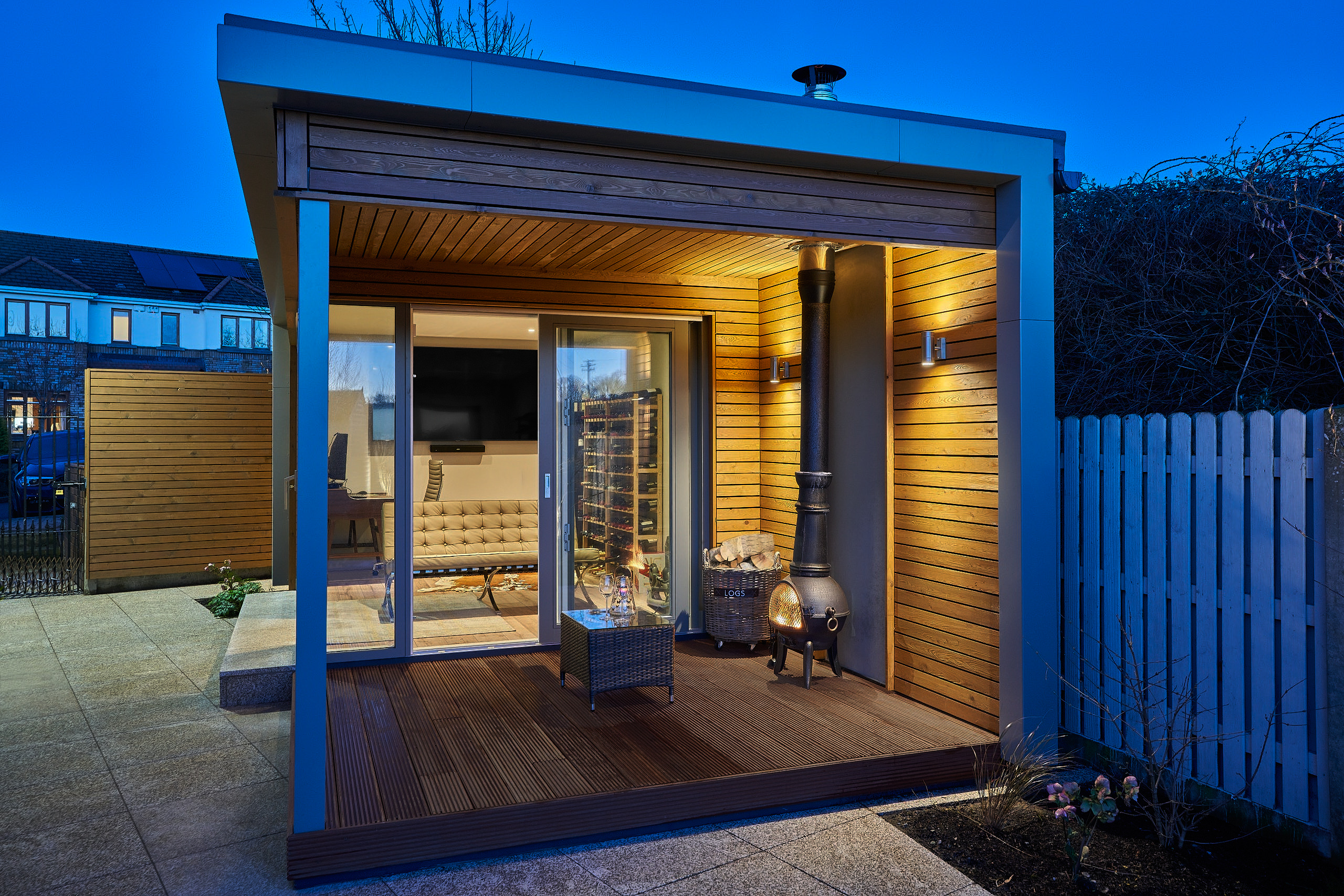 The studio and its covered deck at dusk, the interior lit behind full-height glazing