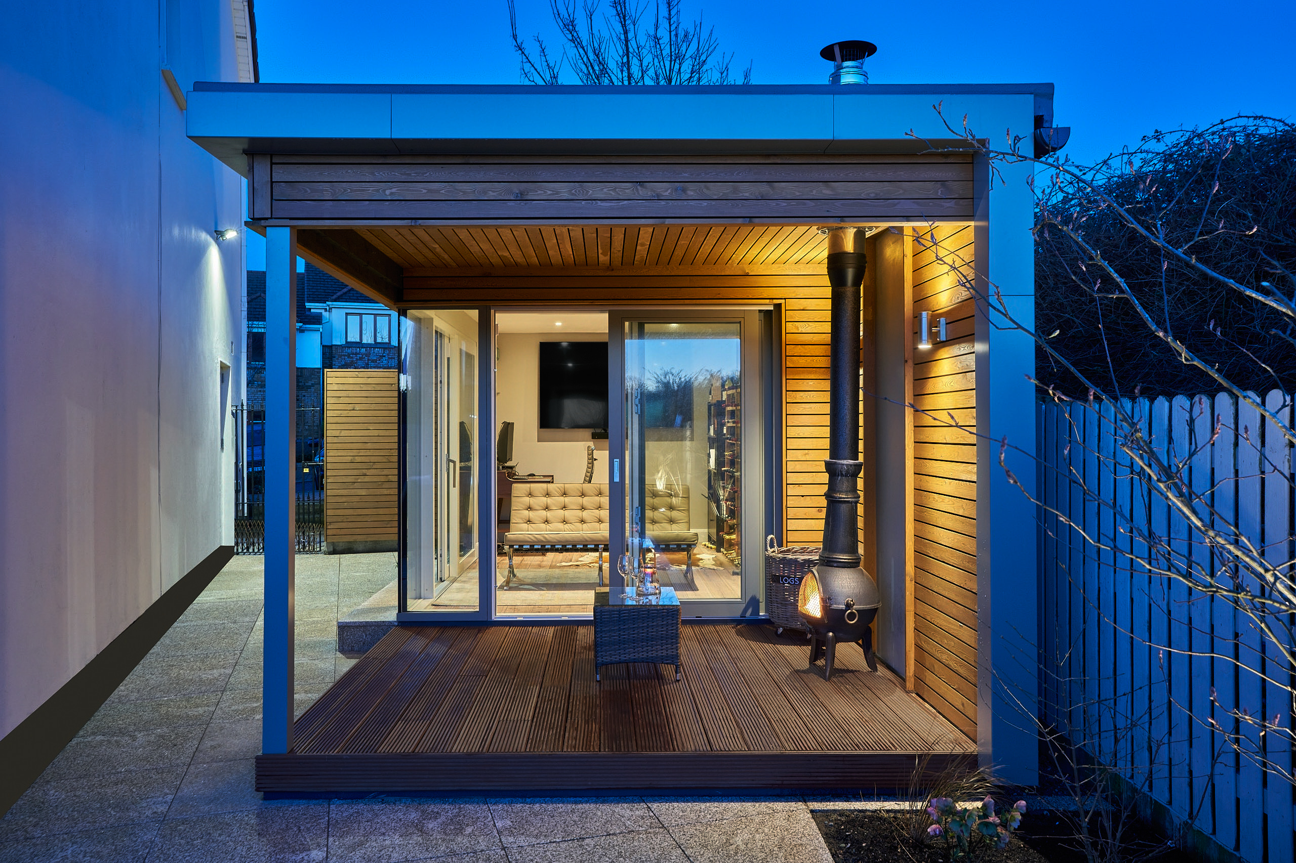 The studio's covered deck at dusk, lanterns lit either side of the glazed doors