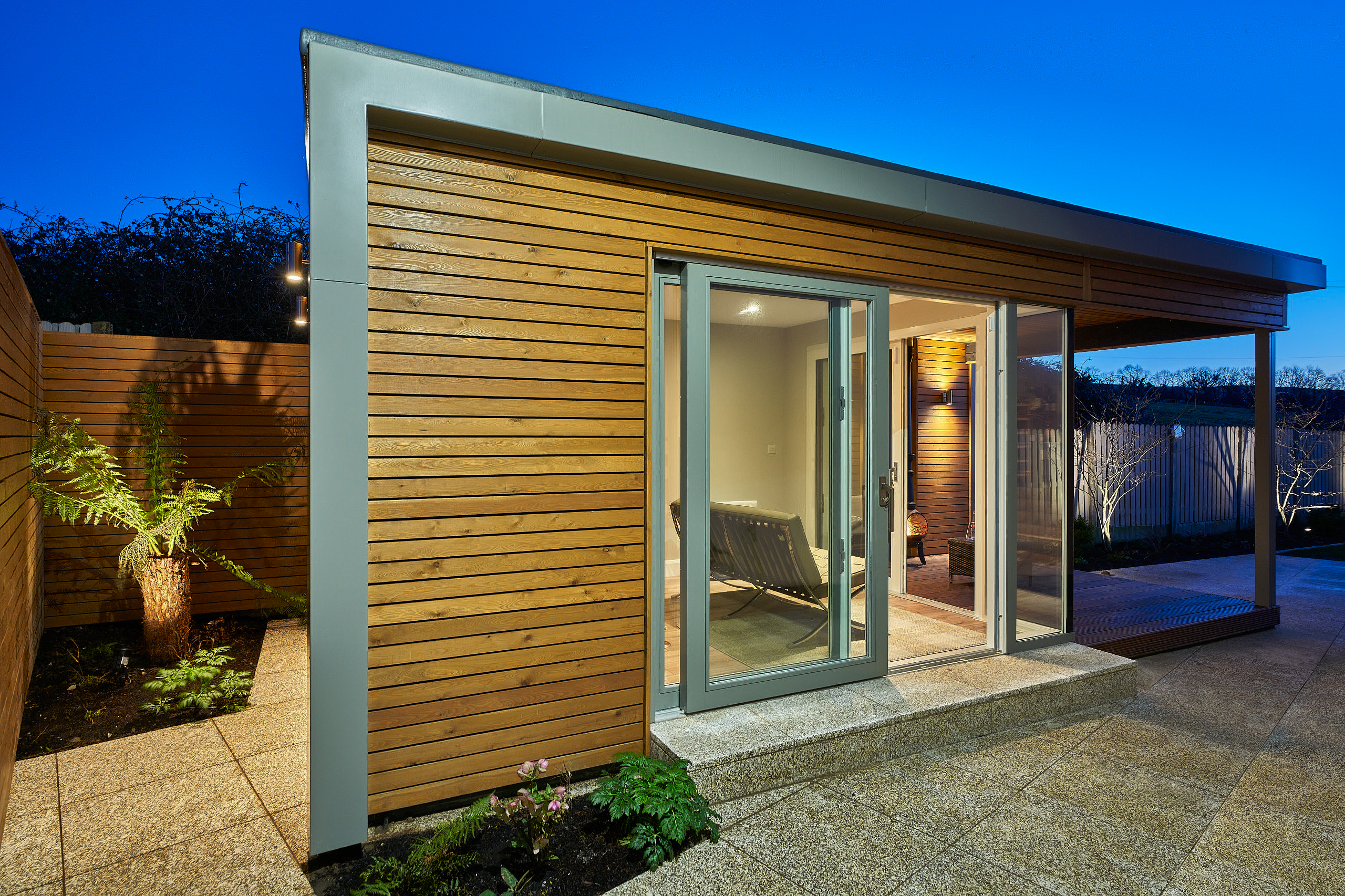 The side of the studio at dusk, cedar cladding running back to the glazed corner