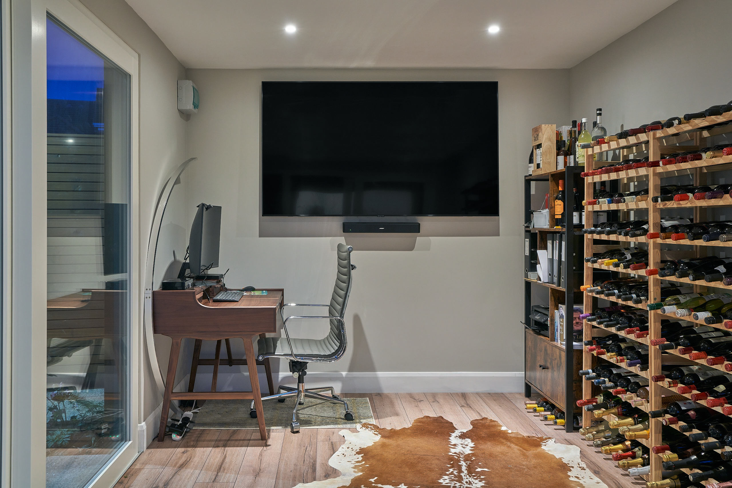 Inside the studio, a desk and office chair beside a full-height wine rack and wall-mounted screen