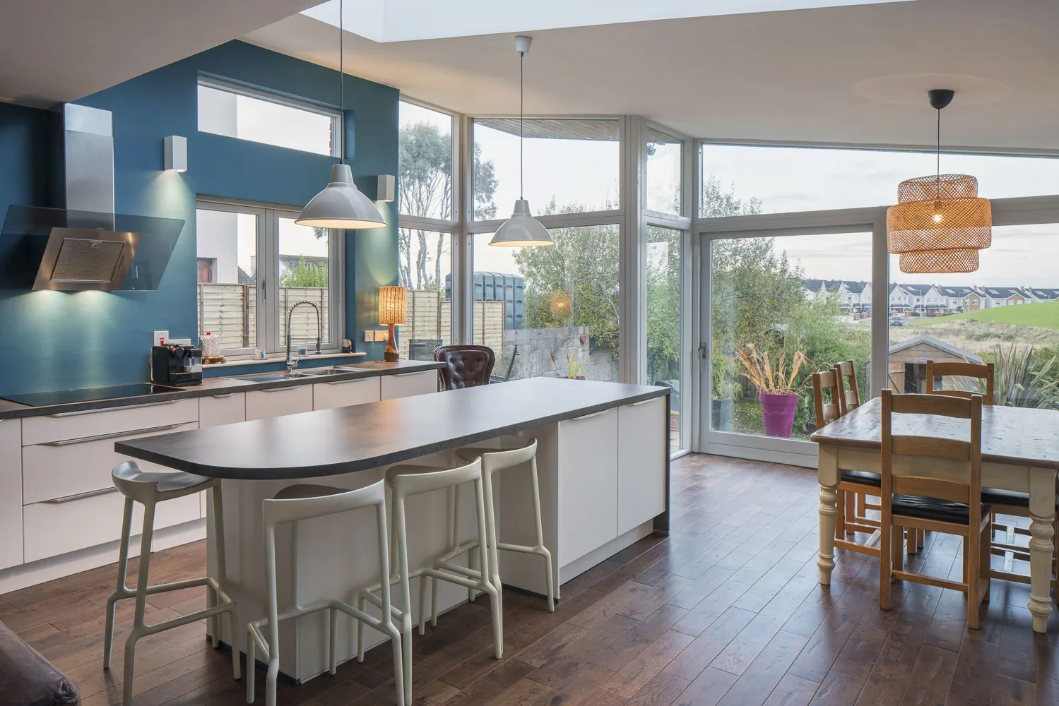 A kitchen with a long curved island and breakfast bar, in an extension with floor-to-ceiling windows