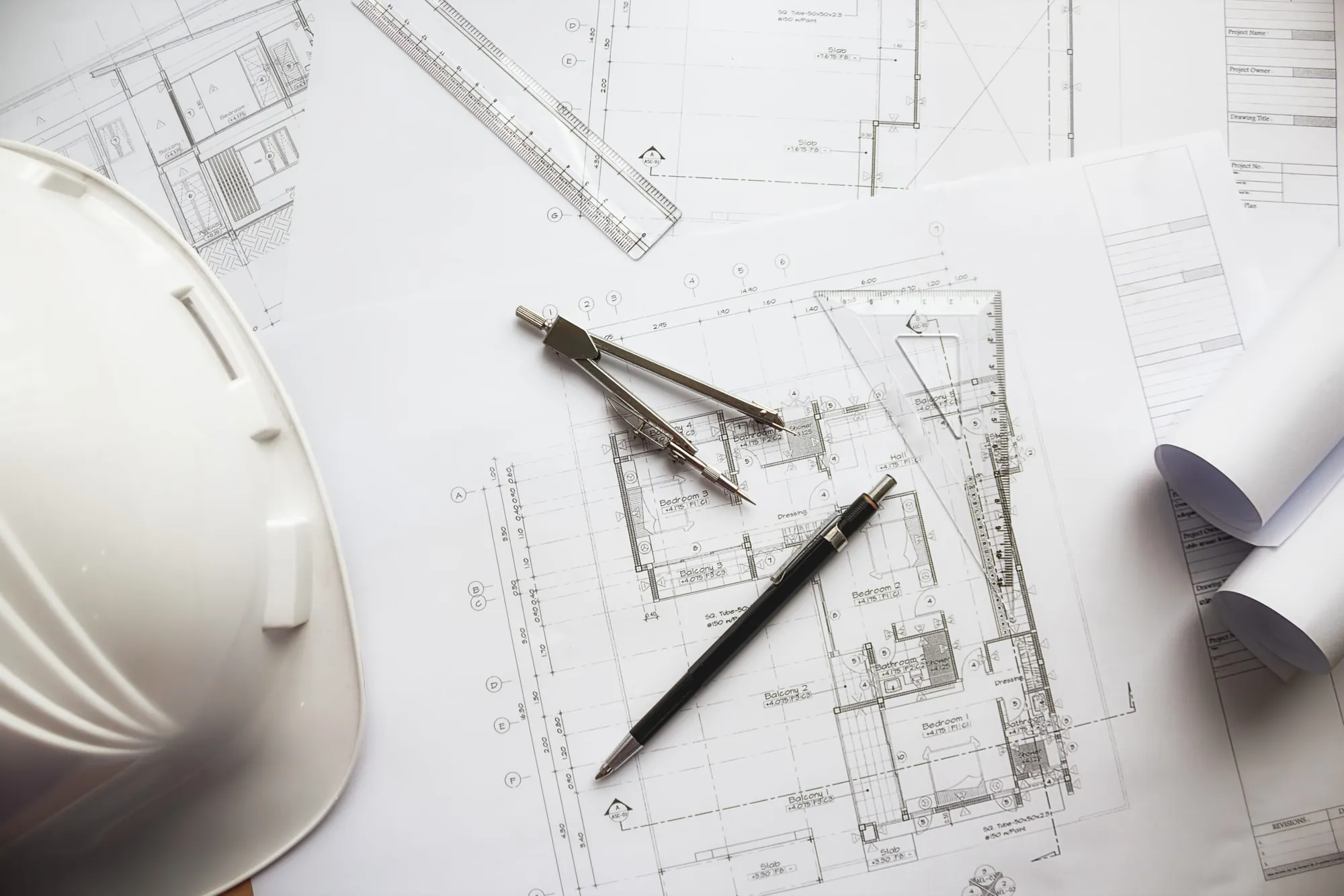 Architectural floor plans on a desk with a hard hat, a compass, a pencil and a ruler