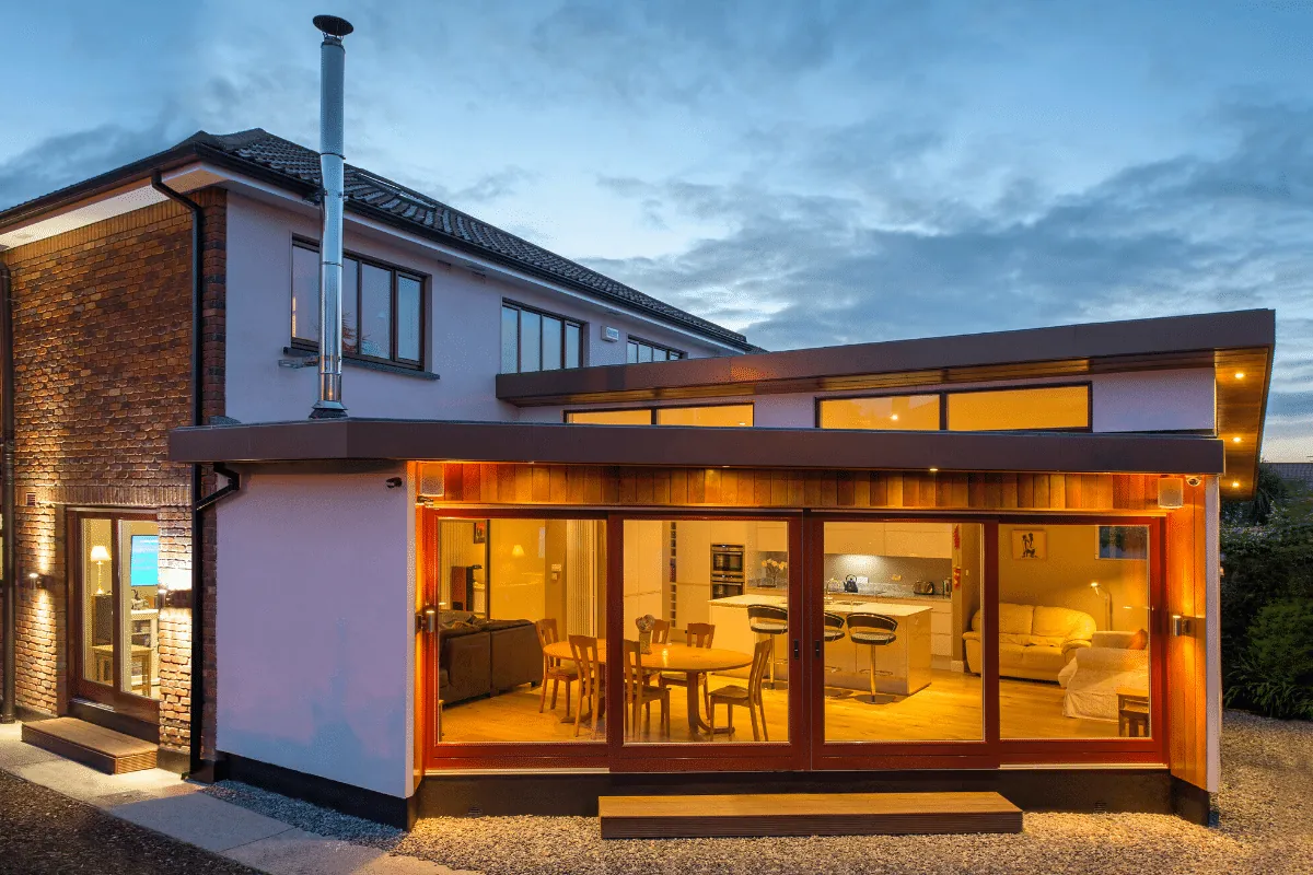 A house extension with clerestory windows above a wall of timber-framed glazing, lit at dusk