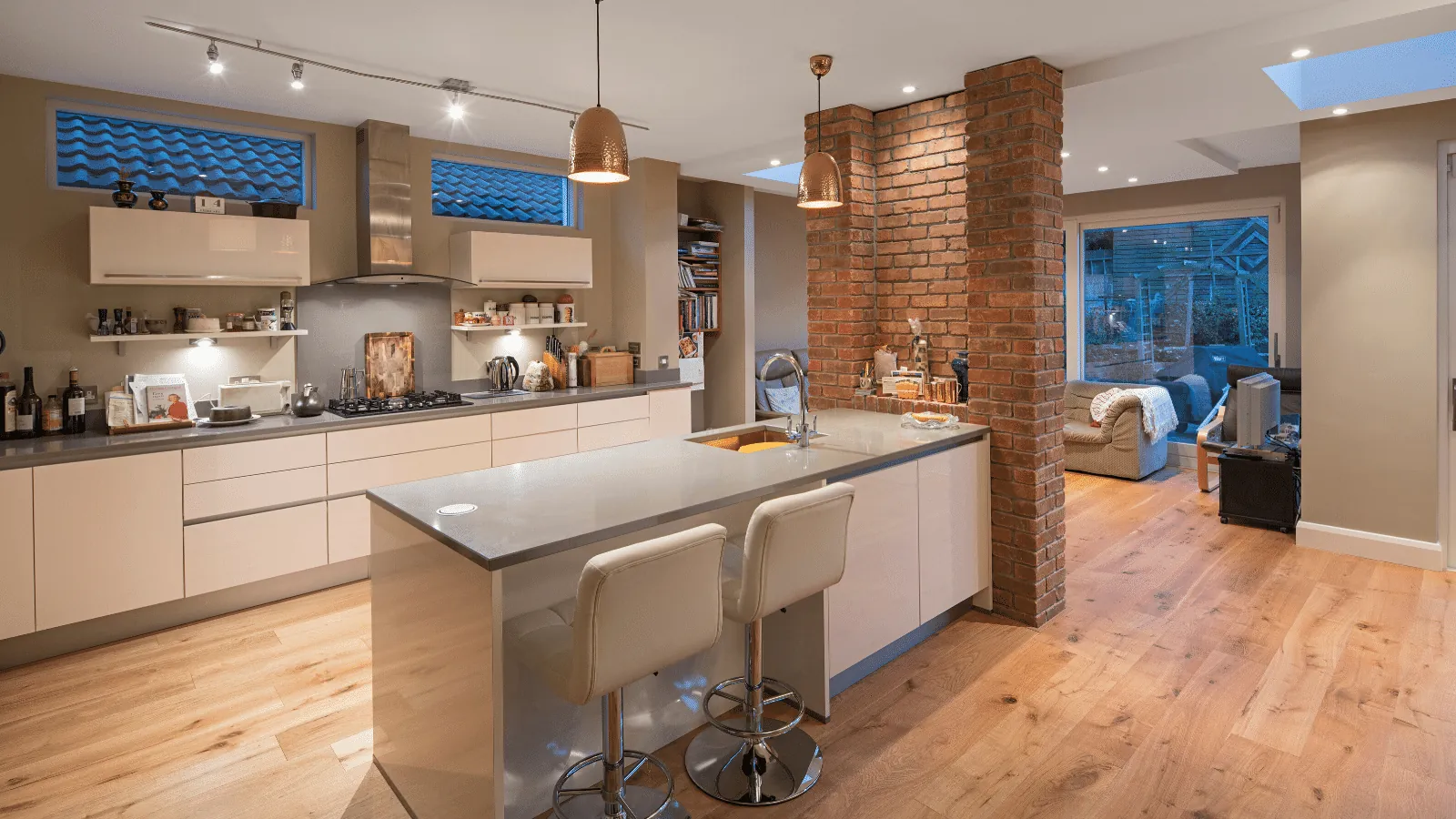 A kitchen with a peninsula breakfast bar and a brick pillar, open to a living area