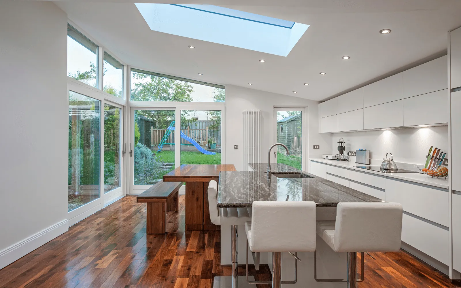 A kitchen extension with a glazed corner, a rooflight, white units and an island with bar stools