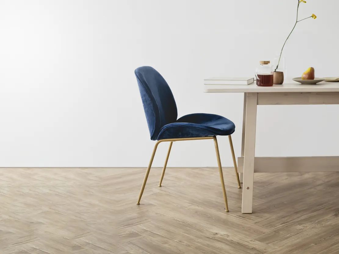 A blue velvet chair at a pale wooden table against a white wall