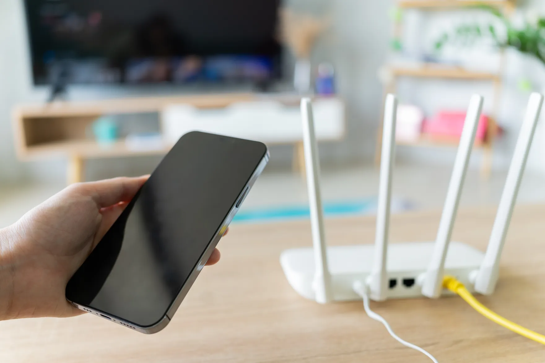 A hand holding a smartphone beside a Wi-Fi router