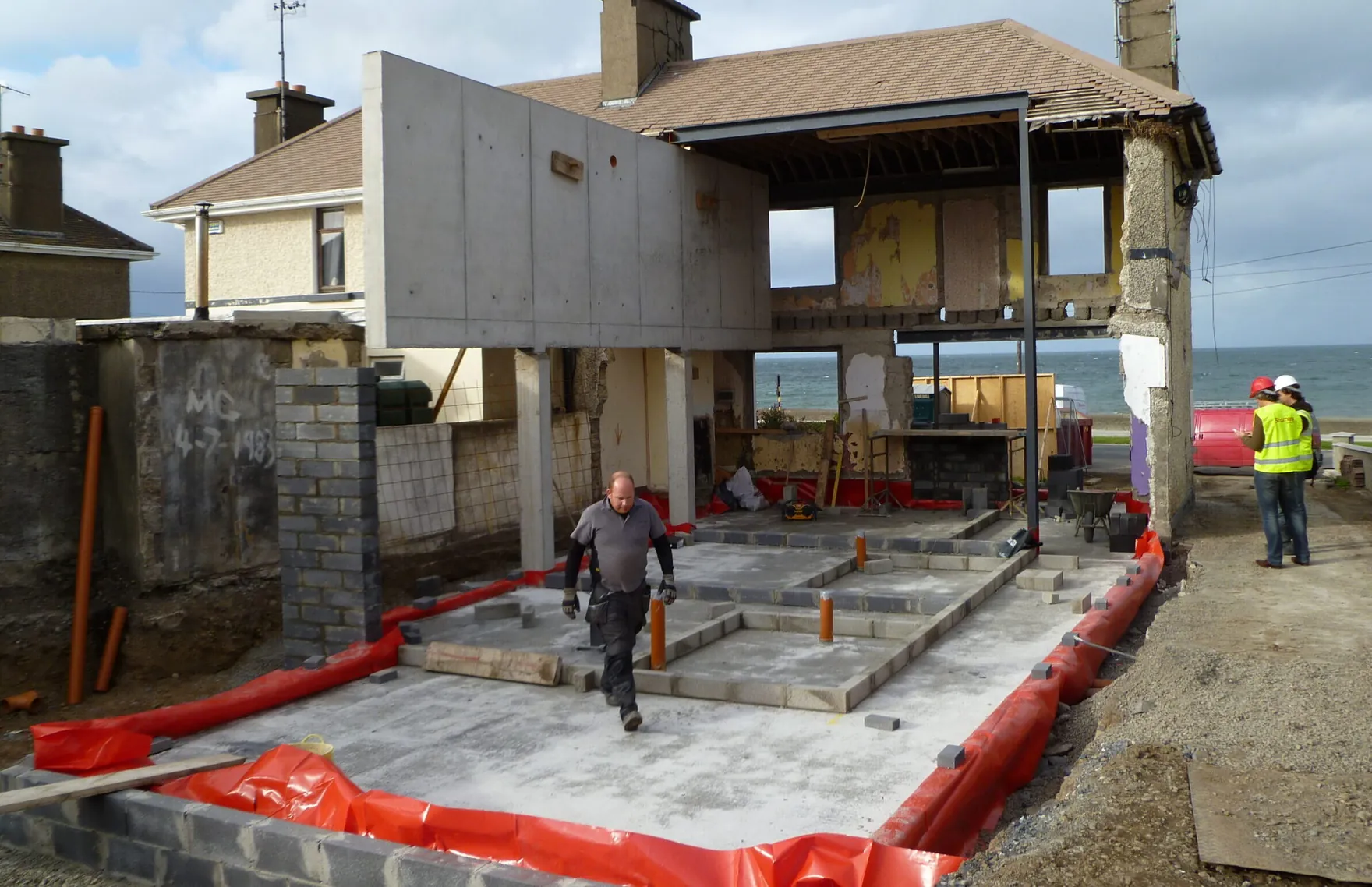 A house extension under construction, with a concrete floor slab and a builder walking across the site