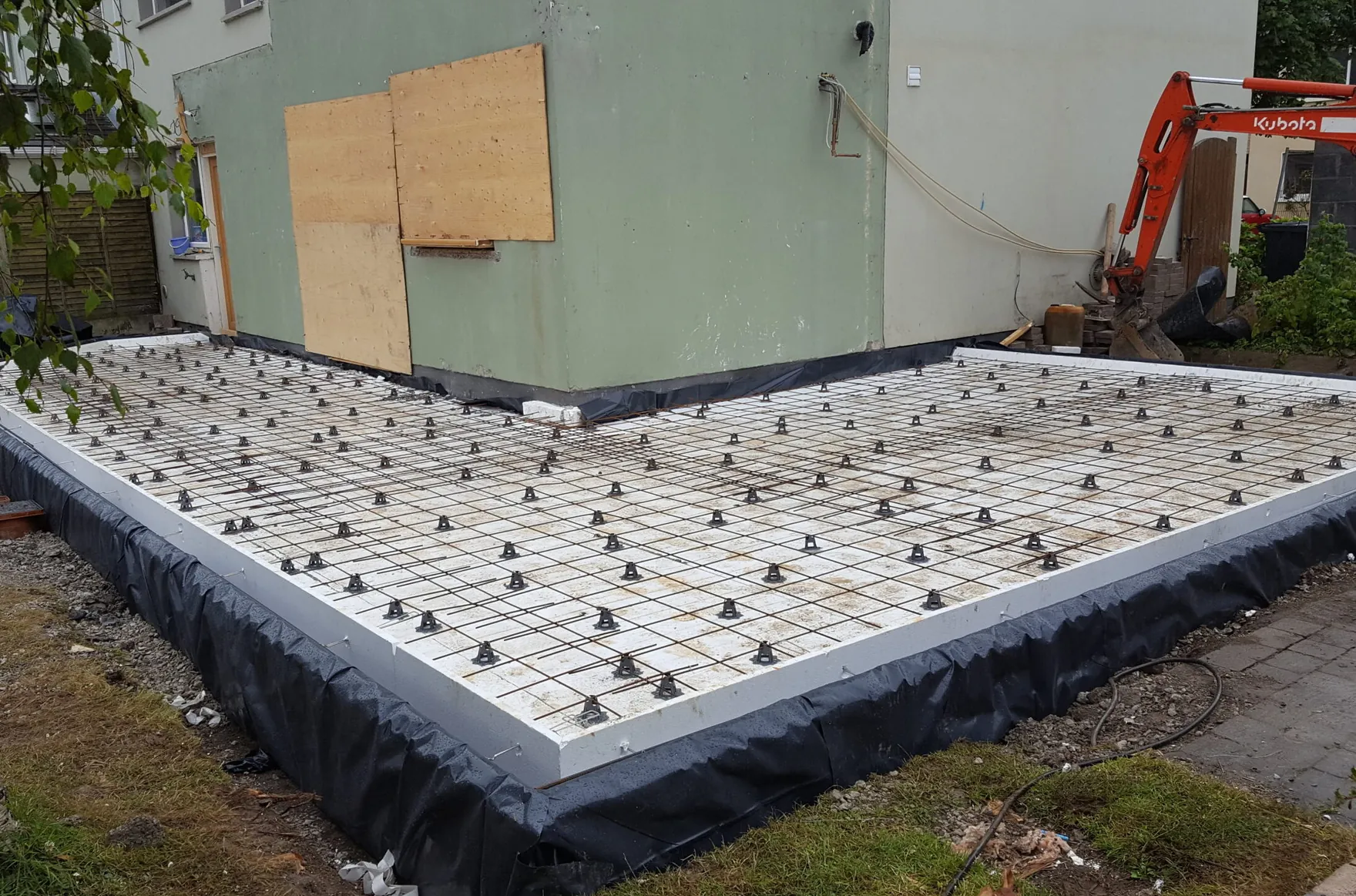 An insulated foundation with steel reinforcement mesh laid beside a house