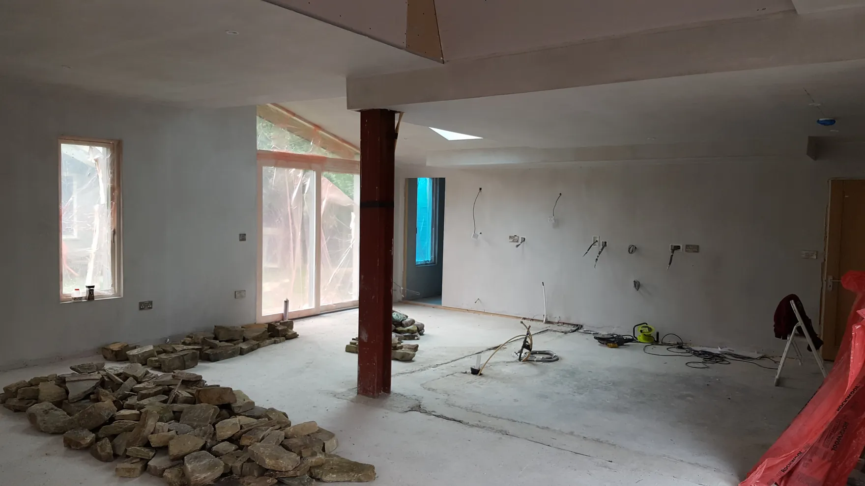 The unfinished interior of a house extension, with plastered walls and a pile of stone on the floor