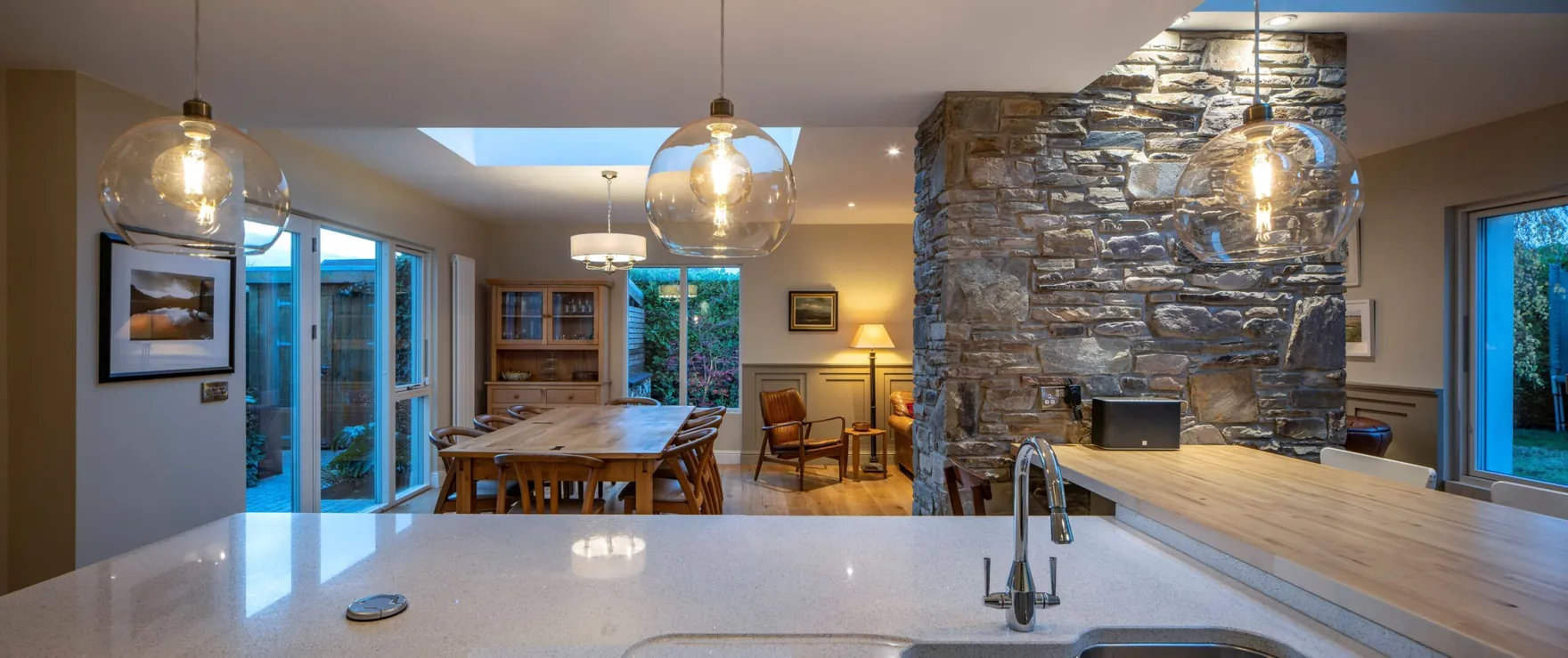 An open-plan kitchen and dining room with glass pendant lights and a stone feature wall