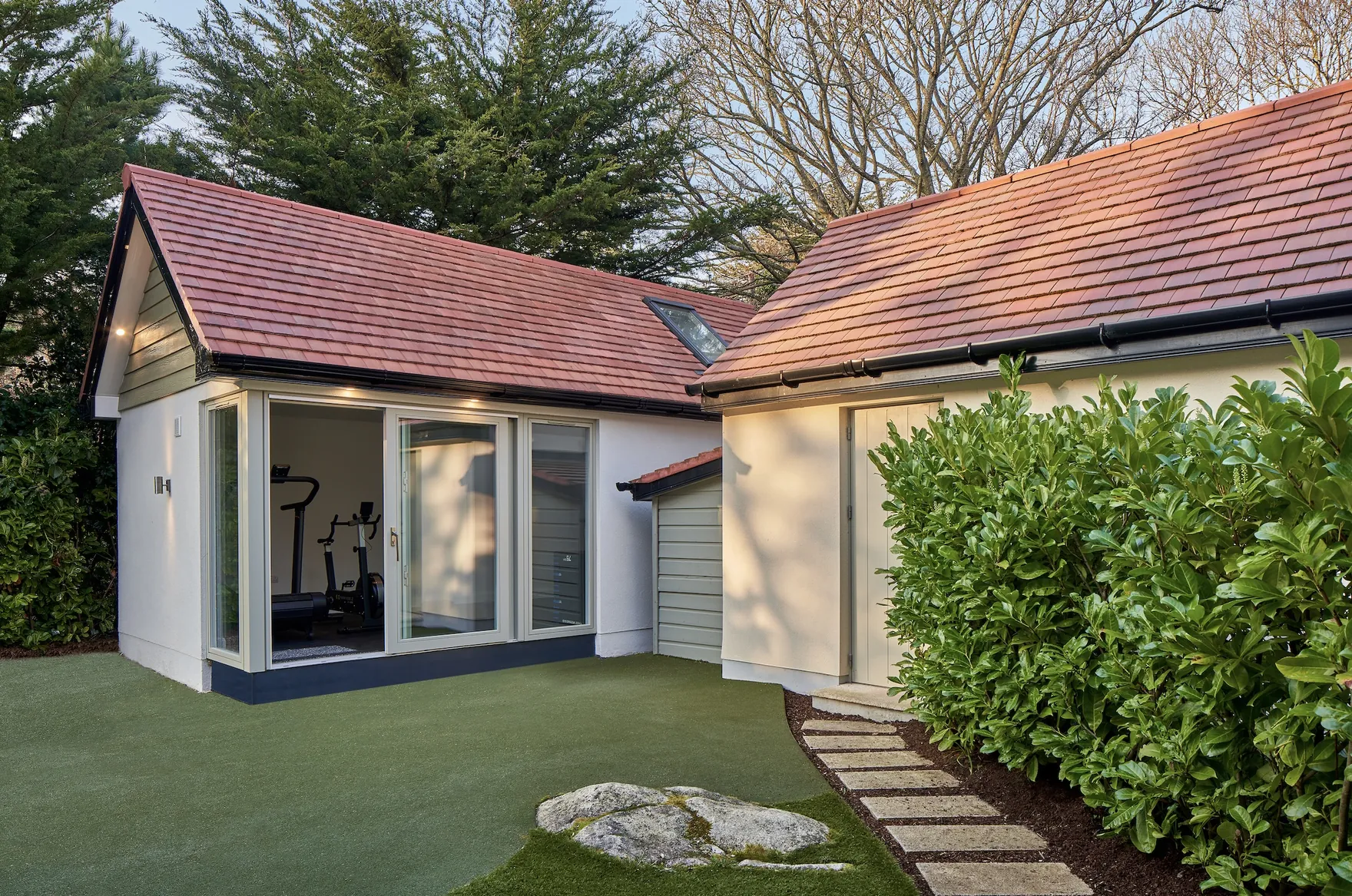 A white rendered building with a tiled pitched roof and glass doors, used as a home gym