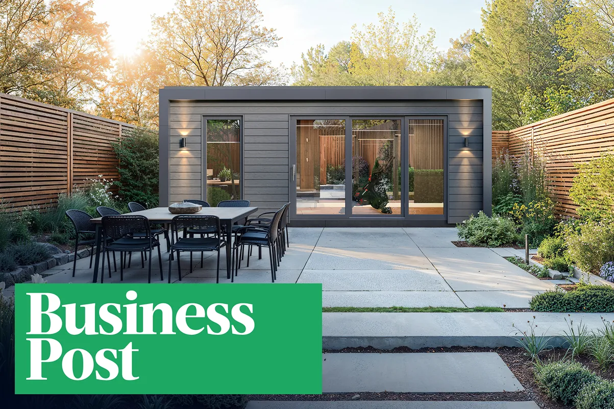 A grey garden studio with glass doors behind a paved patio and dining table, with the Business Post logo