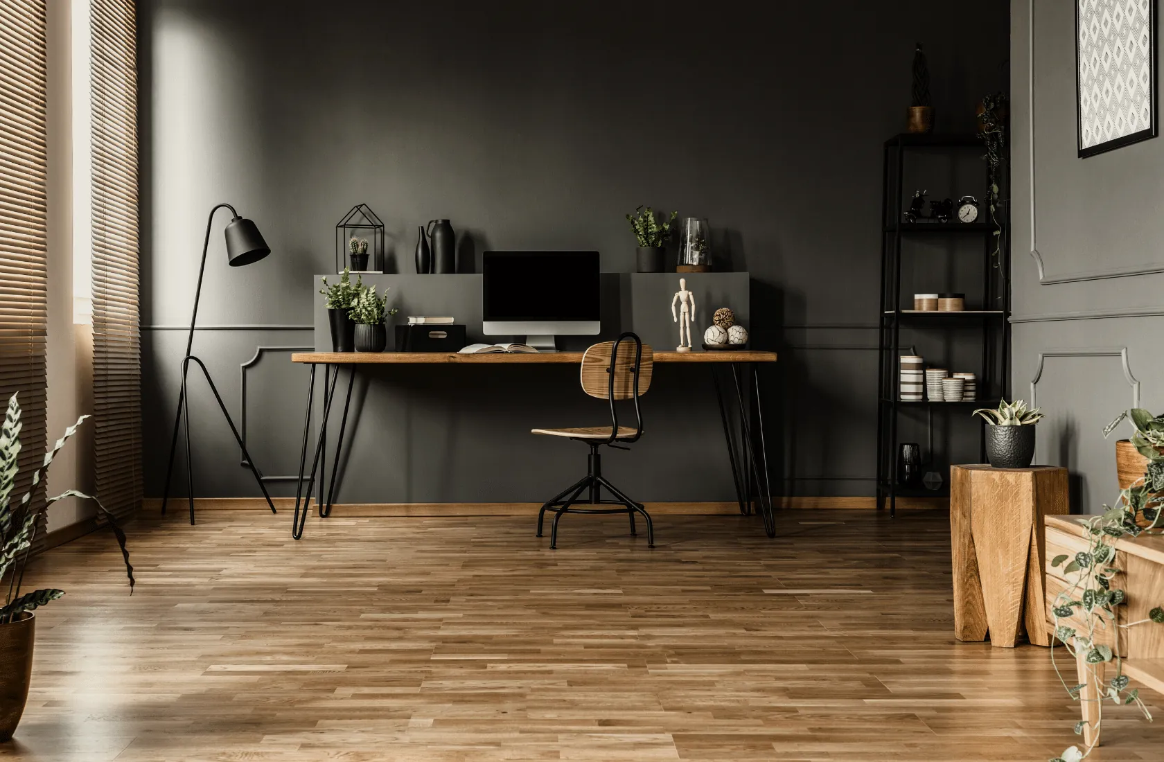 A home office with dark grey walls, a desk with a computer and a wooden chair