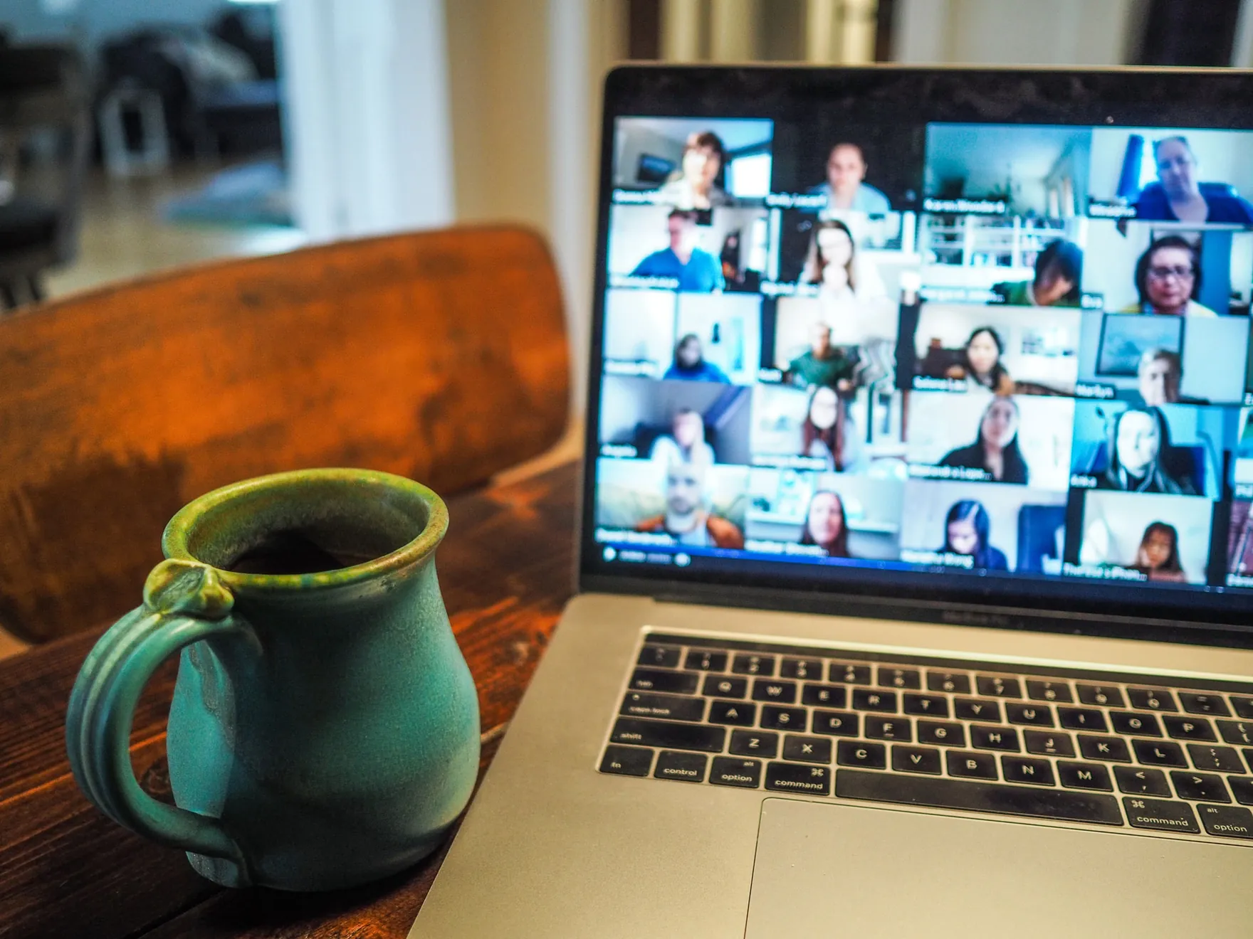 A laptop showing a video call with many participants, beside a ceramic mug