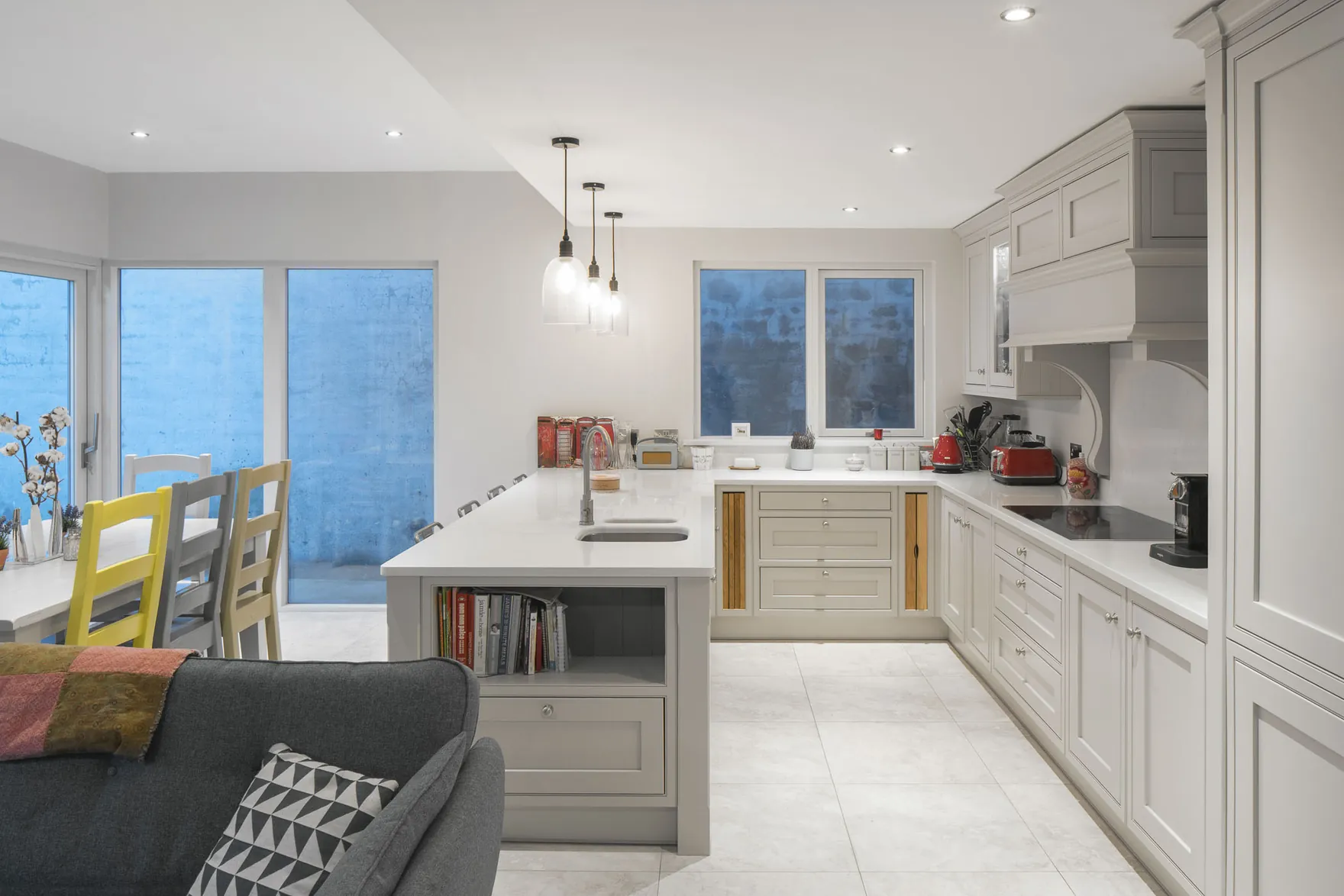 A kitchen with a peninsula counter, pale grey shaker units and glass pendant lights