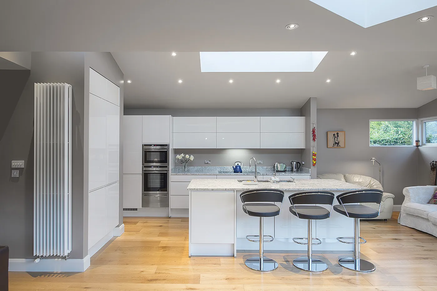A white gloss kitchen with a peninsula breakfast bar, three bar stools and a rooflight