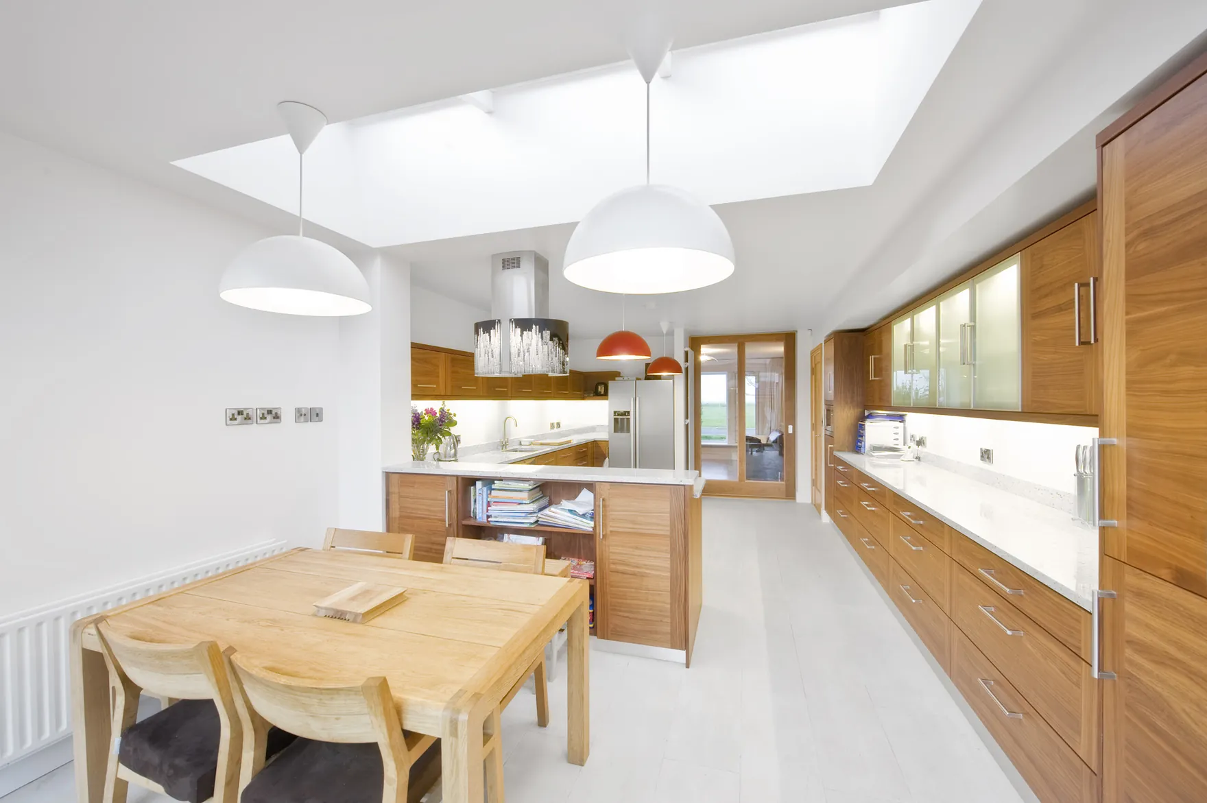 A kitchen and dining area with walnut units and white pendant lights under a large rooflight